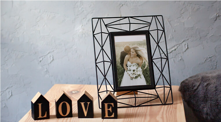 Close up of decorative items, such as photo frame and letters spelling love, on top of a wooden bedside table against a light grey wall